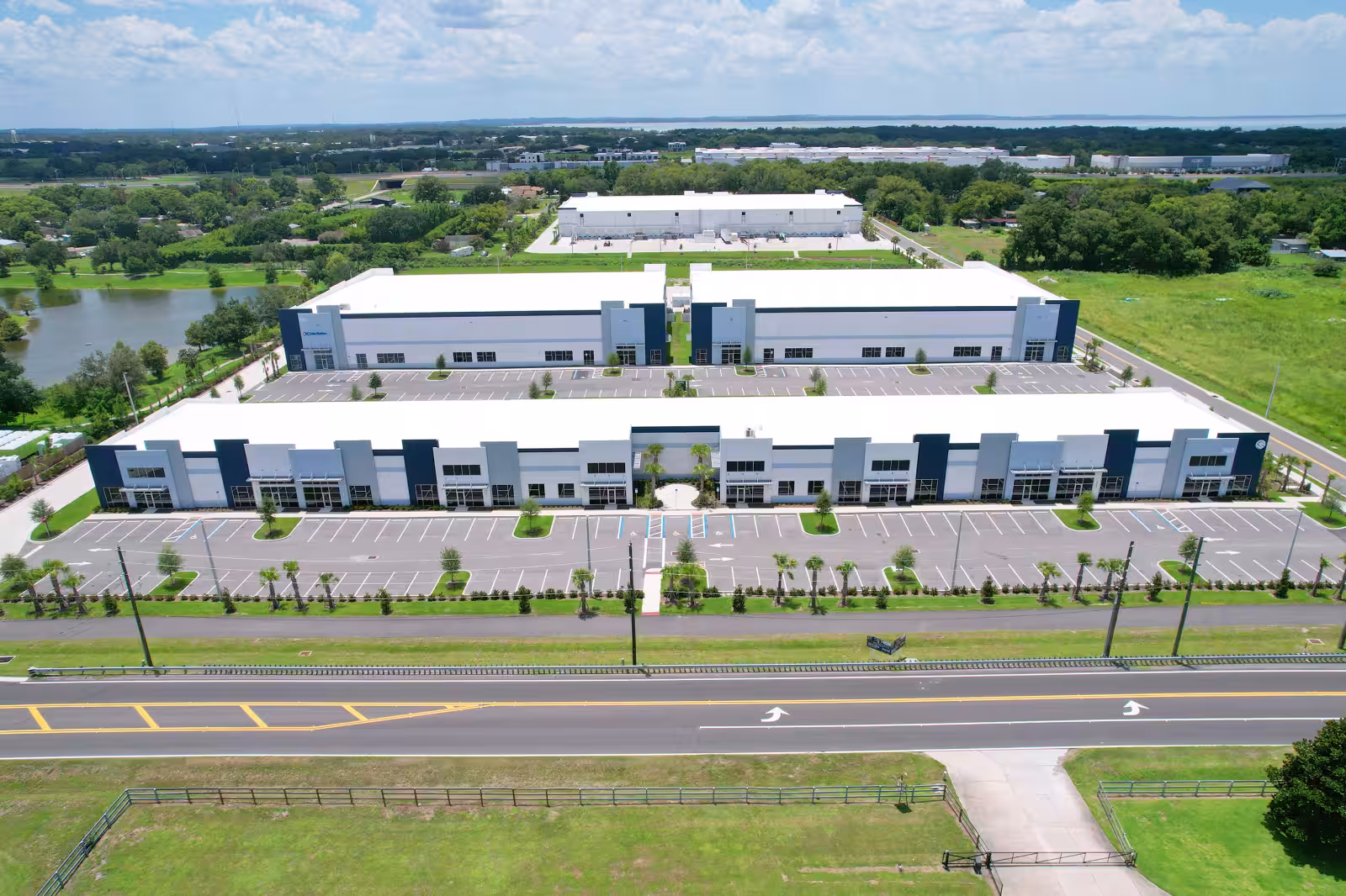 Aerial view of 429 Business Center in Ocoee, Florida: two long navy-and-white flex industrial buildings with storefront entries, flanked by striped parking lots, palm trees, and a divided highway in the foreground.